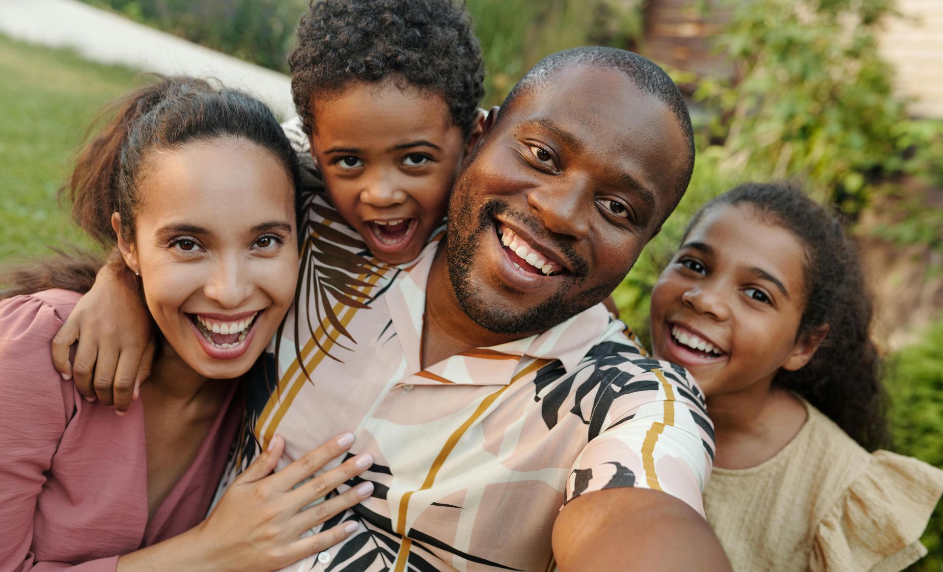 A joyful multicultural family taking a selfie outdoors in a lush garden setting.